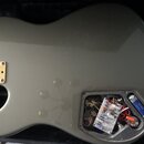 Zadní strana elektrické kytary v šedé barvě. Na kovovém zlatém mostku je nápis Fender Mexico. V otevřeném prostoru elektroniky jsou vidět zapájované…