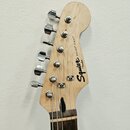 Fotografie zachycuje hlavu světlé dřevěné elektrické kytary s chromovanými ladičkami. Na povrchu je černý nápis Squier by Fender a označení modelu BU…