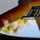 Detailní pohled na spodní část elektrokitary s barevným přechodem od žluté přes červenou k černé. Na těle je instalován kovový kobylník s viditelnými…