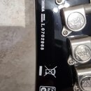 Detail zadní strany hlavy černého nástroje s kovovými ladičkami. Je zde uveden nápis CHINA a SERIAL NUMBER L0702968. Dole je vidět symbol přeškrtnuté…
