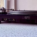 Černý gramofon s černým talířem a hrací jehlou. Na zadní straně je štítek s nápisy STANTON MAGNETICS, INC., MODEL NO. ST 150, AC POWER SUPPLY: ADAPTA…