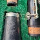 Černý dřevěný nástroj, pravděpodobně klarinet, uložený v zeleném polstrování. Na zvonu je vyryto logo s nápisy SELMER PARIS, SOLE AGENTS H.A. CAN a n…