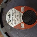 Fotografie zachycuje zadní stranu reproduktoru s kovovým rámem a šedým magnetem. Na magnetu je nalepený oválný štítek s bílou a červenou částí, na kt…