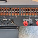 Zadní strana černého rackového zesilovače s ventilační mřížkou. Jsou zde viditelné nápisy BALANCED INPUTS, SPEAKER OUTPUTS, LINK CH B a LINK CH A. U…