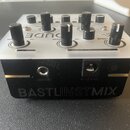 Černý mixovací přístroj s bílým horním panelem a několika černými otočnými knoflíky. Na přední straně je nápis BASTLINSTMIX a konektory s popisky MIX…