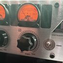 Detailní pohled na stříbrný přední panel studiového zařízení. Jsou vidět dva analogové VU metry s oranžovým pozadím a nápisy COLD, WARMTH, WARM, BEHR…