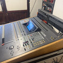 Šedočerný digitální mixážní pult umístěný v dřevěném transportním kufru. Na pravé straně je vidět bílý nápis „O2R DIGITAL RECORDING CONSOLE“. V horní…