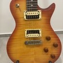 Elektrická kytara s trupem v žlutě-oranžovém sunburst provedení a viditnou strukturou dřeva. Nástroj má dva humbuckery s krémovými rámečky, čtyři hně…