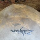 Detailní pohled na povrch mosazného činele. Na ploše je vidět tmavý nápis Zildjian. Povrch vykazuje výrazné oxidace, skvrny a známky opotřebení.