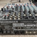Fotografie zachycuje míchací pult stříbrné barvy s množstvstvím potenciometrů a tlačítek. Na horní části je vidět nápis BEHRINGER XENYX X1204USB. Na…