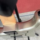 Detailní pohled na spoj krku a těla elektrické kytary v stříbrné barvě. Krk je vyroben ze světlého dřeva s viditelnou masivností. Spojení těla a krku…