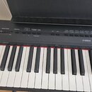 Detailní pohled na ovládací panel a klávesy digitálního piana černé barvy. Na pravé straně je bílé logo YAMAHA. Panel obsahuje řadu tlačítek a posuvn…