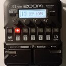 Černý multi-efektový procesor značky ZOOM, model G1 FOUR. Na displeji je zobrazen nápis 11 ZEP 1959. Zařízení má čtyři ovládací knoflíky s popisky Lo…