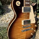Elektrická kytara s trupem v tmavě hnědé barvě s výraznou dřevěnou strukturou a krémovým lemováním. Nástroj má dva humbuckery s krémovými rámečky, kr…