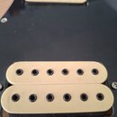 Fotografie zachycuje dva elektrokytarové snímače s krémovými plastovými kryty v černém pickguardu. Spodní snímač je typu humbucker se dvěma řadami še…
