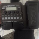 Černý multi-efektový procesor s integrovaným pedálem. Na horní části je nápis A1X FOUR, logo ZOOM a text Multi-Effects Processor. Zařízení obsahuje d…