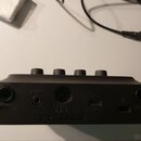 Zadní strana černého kompaktního efektového pedálu nebo mixéru s čtyřmi ovládacími knoflíky na horní hraně. Na zadním panelu jsou vidět konektory s p…