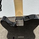 Zadní strana černé elektrické kytary s krčkem z přírodního dřeva. Na kovém spojovacímdesce mezi krčkem a tělem je vyryto logo Fender. Povrch kytary j…