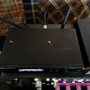 Černý bezdrátový přijímač s dvěma anténami a digitálním displejem. Na pravé straně předního panelu je nápis SENNHEISER a nad ním ovratový knoflík s o…