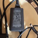 Černý síťový adaptér s napojeným kabelem a konektorem. Na štítku je uveden text Class 2 Power Supply AC ADAPTOR, MODEL(型号):CW1203000, INPUT(输入):100-2…