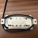 Elektrický snímač kytary v bílé barvě s kovovými montážními úchyty. Na povrchu je nápis „Seymour Duncan“ a text „Made in America“. V horní části je n…