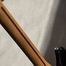 Detail zadní strany krku kytary vyrobeného ze světlého dřeva s dvěma tmavšími pruhy. Povrch je lakovaný a hladký. V pravé dolní části je vidět černá…
