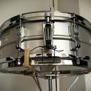 Stříbrný snare drum s chromovanými obručemi a mechanismem. Na korpusu je vidět logo „Ludwig“ v modro-žlutém rámečku a na mechanismu napnutí je nápis…