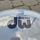 Fotografie zachycuje průhledný plastový buben s černým logem. Na povrchu je nápis drums a pod ním stylizovaný symbol DW. Povrch vykazuje drobné škráb…
