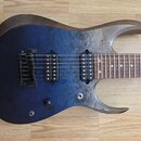 Elektrická kytara s modrým průsvitným lakem na těle, pod kterým je vidět struktura dřeva. Nástroj má dva humbuckery a pevný most s pružinami. Na hmat…