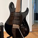 Černá elektrická kytara s hnědým hmatníkem a třemi snímači typu humbucker. Na ovládacích knoflících jsou nápisy VOLUME a TONE. Nástroj je umístěn na…