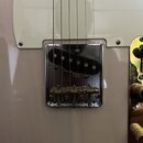Detail elektrické kytary s bílým pickguardem a chromovaným snímačem. Na krytu snímače je nápis „In-Tune!“ a pod ním menší, nečitelný text. Pod snímač…