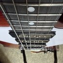 Detail hmatníku elektrické kytary s tmavým dřevěným povrchem a dvěma bílými kulatými polohovými značkami. Je vidět černý humbucker s viditelnými póly…