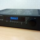 Černý digitální zesilovač s nápisem Apart CONCEPT 1 PROFESSIONAL DIGITAL CONTROLLED AMPLIFIER. Na předním panelu je modrý displej s textem Source A,…