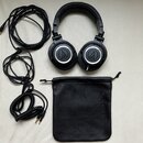 Černá uzavřená velká sluchátka s bílými kroužky kolem centerXů. Na vnější straně obou mušlí je logo Audio-Technica a na horní části náušníků nápis AT…