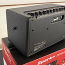 Černý kytarový kombozesilovač s texturovaným povrchem, umístěný na červené krabici s nápisem Spark40 THE SMART WAY TO PLAY AND JAM. Na zadním panelu…