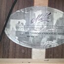 Fotografie zachycuje vnitřek akustického nástroje s přilepeným oválným štítkem a čtvercovým kontrolním lístkem. Na štítku je logo Maton a nápisy HAND…
