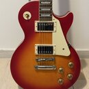 Elektrická kytara s červeno-oranžovým sunburst povrchem a krčkem z tmavého dřeva s trapezoidními vložkami. Nástroj má dva humbuckery, krémový pickgua…