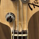 Detail hlavy basové kytary z přírodního dřeva s chromovanými kolíky. Na dřevě je vidět černé logo Fender a v místě přechodu hlavy do hmatníku je výra…