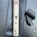 Kondenzátorový mikrofon stříbrné barvy s kovovou síťkou a červeným prstenem v horní části. Na těle jsou nápisy BATT. CHECK, logo AKG, označení C 1000…