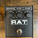 Černý efekt pedál v kovovém krytu s texturovaným povrchem. Na horní části jsou tři černé ovládací knoflíky s nápisy DISTORTION, FILTER a VOLUME. Upro…