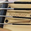 Detailní záběr na kovový mostek zlaté barvy s nápisem Roadstar. Přes mostek vedou čtyři struny, které jsou v části u pražců omotány černým materiálem…