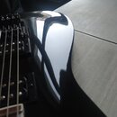 Detailní pohled na černý, vysoce lesklý trup basové kytary. Na snímači je viditelné bílé logo "Epiphone". Povrch nástroje je čistý s výraznými odlesk…