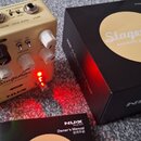 Kremově bílý kytarový předzesilovač s ovládacími knoflíky a přepínači. Na přístroji je nápis Stageman acoustic preamp+DI a logo NUX. Vedle přístroje…