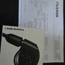 Fotografie zobrazuje krabici od sluchátek a fakturu. Na bílé krabici je zobrazen černý šupen a nápisy „audio-technica“ s logem, „ATH-E40“ a text „PRO…