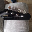 Fotografie zachycuje hlavu černé basové kytary s nápisem Epiphone v žluté barvě. Na hlavě jsou čtyři chromované ladičky. Povrch lakovaného černého dř…