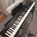 Černý digitální klavír na černém kovovém stojanu. Na levé straně korpusu je bílý nápis CASIO a uprostřed nad klávesami nápis Privia. Nástroj je dopln…