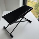 Černý skládací stojan na noty nebo tablet s obdélníkovou plochou a kovovou konstrukcí. Povrch je voorziený svislými žebrovanými drážkami. Na předmětu…