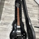 Černá elektrická kytara v otevřeném černém tvrdém pouzdře. Na hlavě hmatníku je bílý nápis Epiphone. Nástroj má dva humbuckery, čtyři ovládací knoflí…
