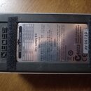 Fotografie zachycuje spodní stranu efektového pedálu s kovovým šedým povrchem. Na zařízení je nalepený informační štítek s nápisy BOSS AC ADAPTOR, Dr…