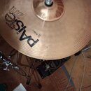 Kovový činel v medově hnědé barvě s viditelným rýhováním povrchu. Na povrchu je černý nápis PAISTE, pod kterým je menší text "THE GENIAT" a označení…